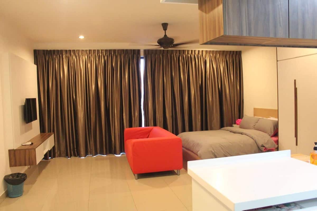 Une chambre d’hôtel avec un lit, une chaise rouge, une table blanche, un téléviseur et un ventilateur de plafond.