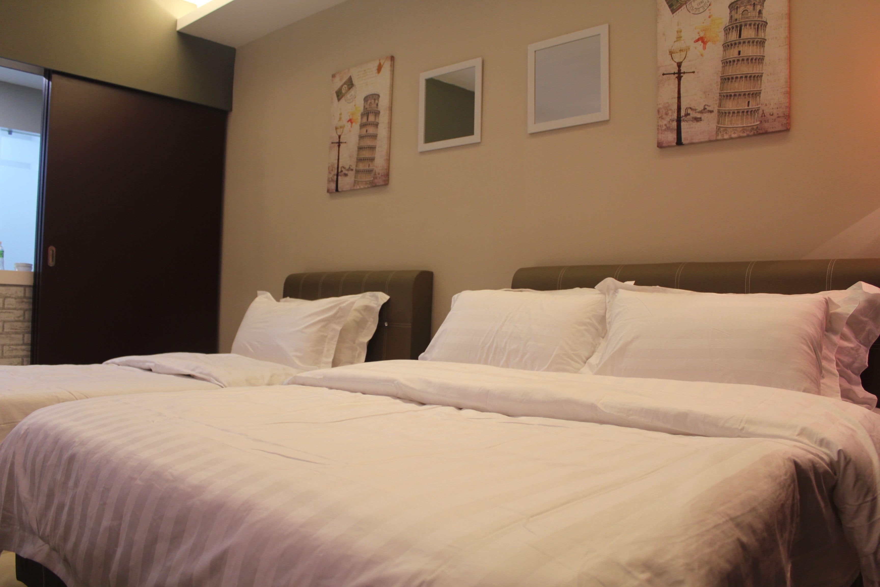 A hotel room with two beds, a dark wooden headboard, and three wall-mounted paintings of the Leaning Tower of Pisa.