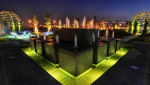 Un espace extérieur aménagé pour la nuit, avec une fontaine centrale entourée de structures et d’arbres illuminés.
