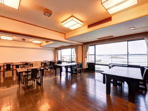 A spacious dining area with wooden tables and chairs, large windows offering a view of the sea, and modern lighting fixtures. - Taikairou (Minamichita)
