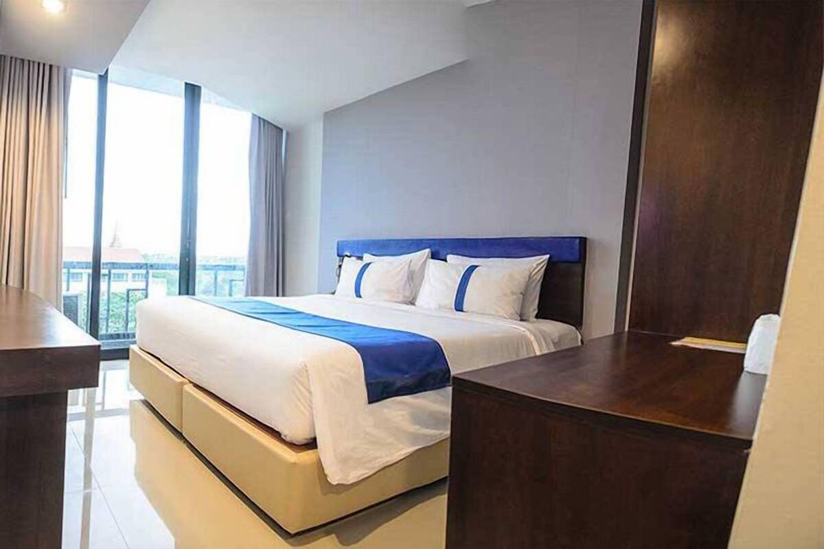 Una habitación de hotel moderna con una cama grande, un escritorio de madera y vistas de la ciudad a través de amplios ventanales.