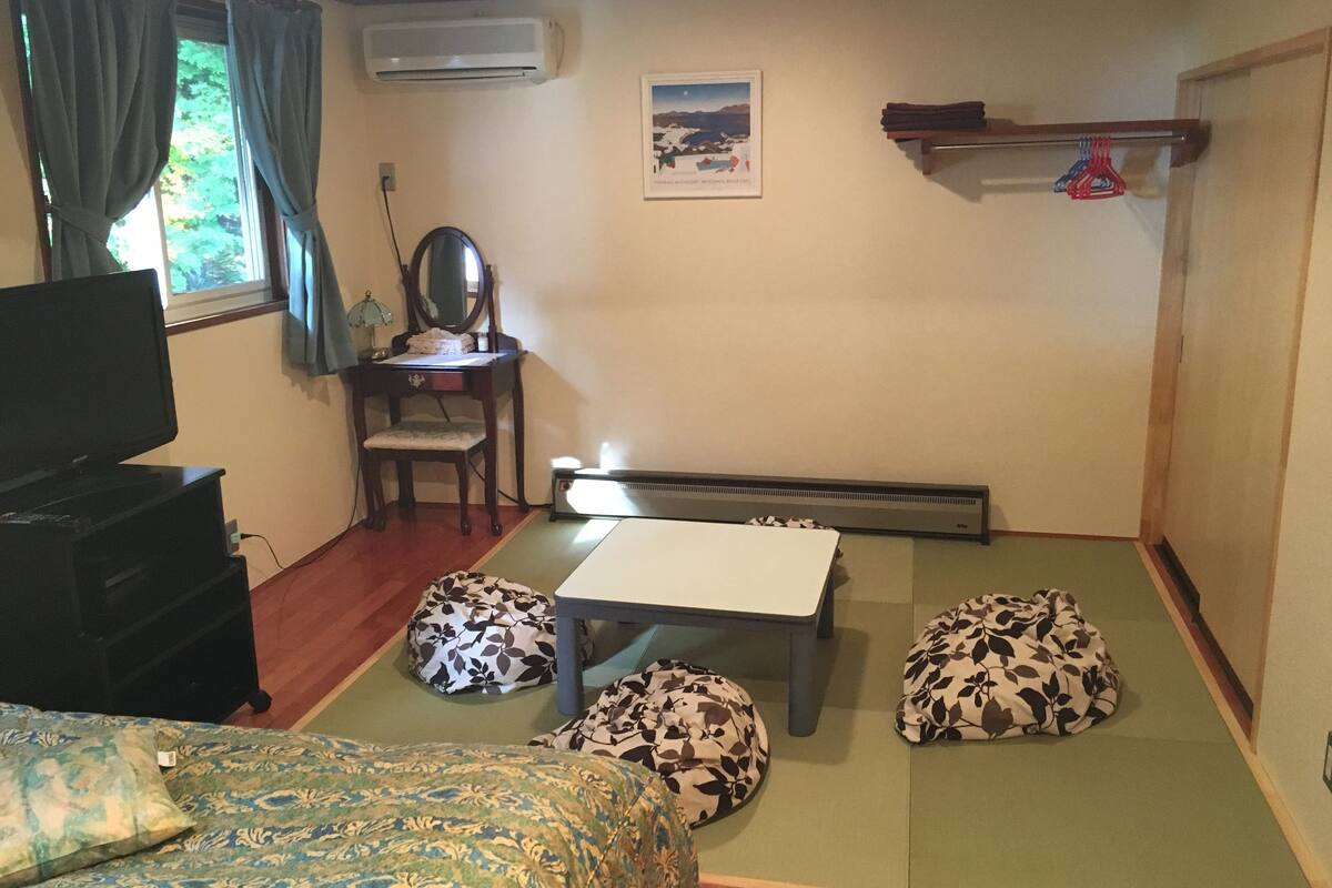 A room with a bed, a desk, a chair, a radiator, and a window with curtains.