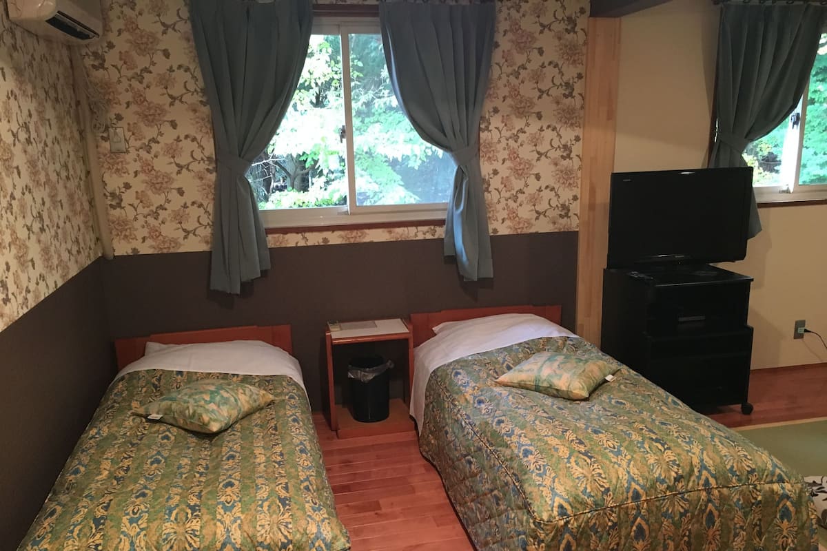 A room with two beds, a small table, a trash bin, and a TV stand.