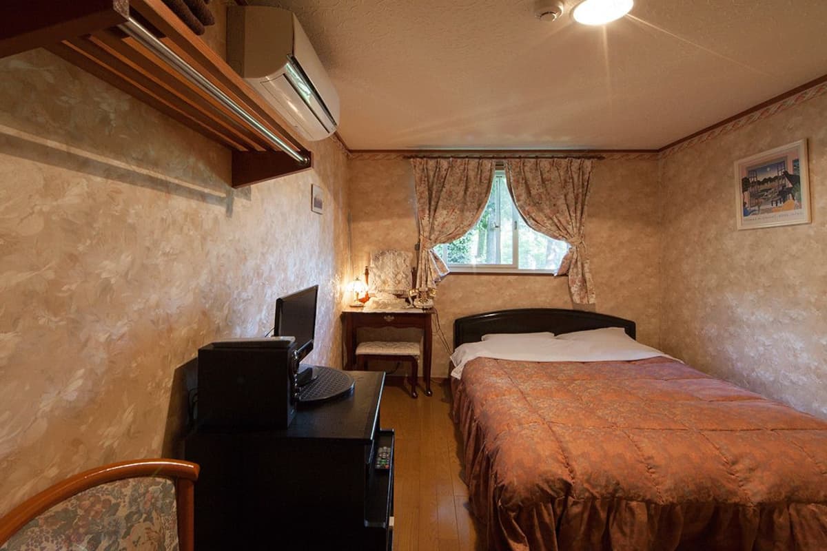 A compact hotel room with a bed, a desk with a computer, a chair, and a window with curtains.