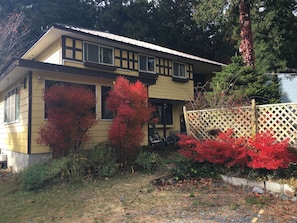 A two-story house with a yellow exterior and black trim, surrounded by a wooden fence and red foliage. - Friendly Inn People (Fujikawaguchiko)