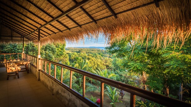 A covered outdoor area with a thatched roof, wooden benches, and a view of a lush landscape. - Good Time Sports Village (Ko Mak)