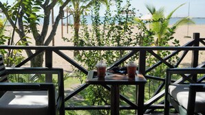 A wooden deck with a table and chairs, overlooking a beach with palm trees and a clear sky. - Bann Pae Cabana (Rayong)