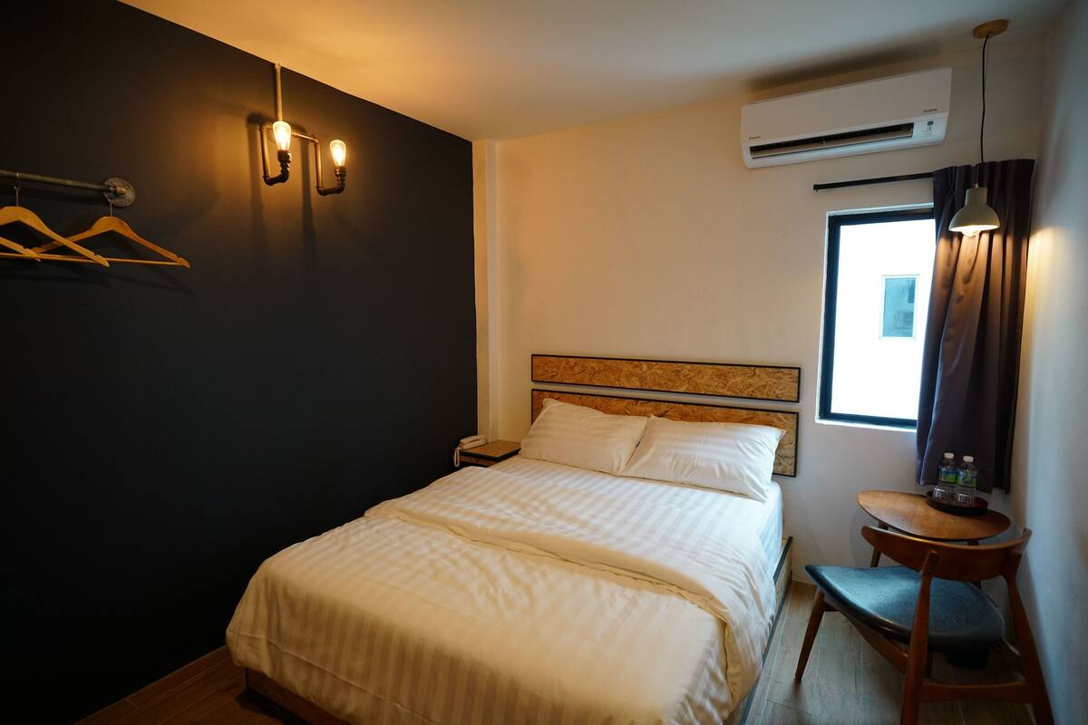 A hotel room with a bed, bedside table, and a small table with bottles.