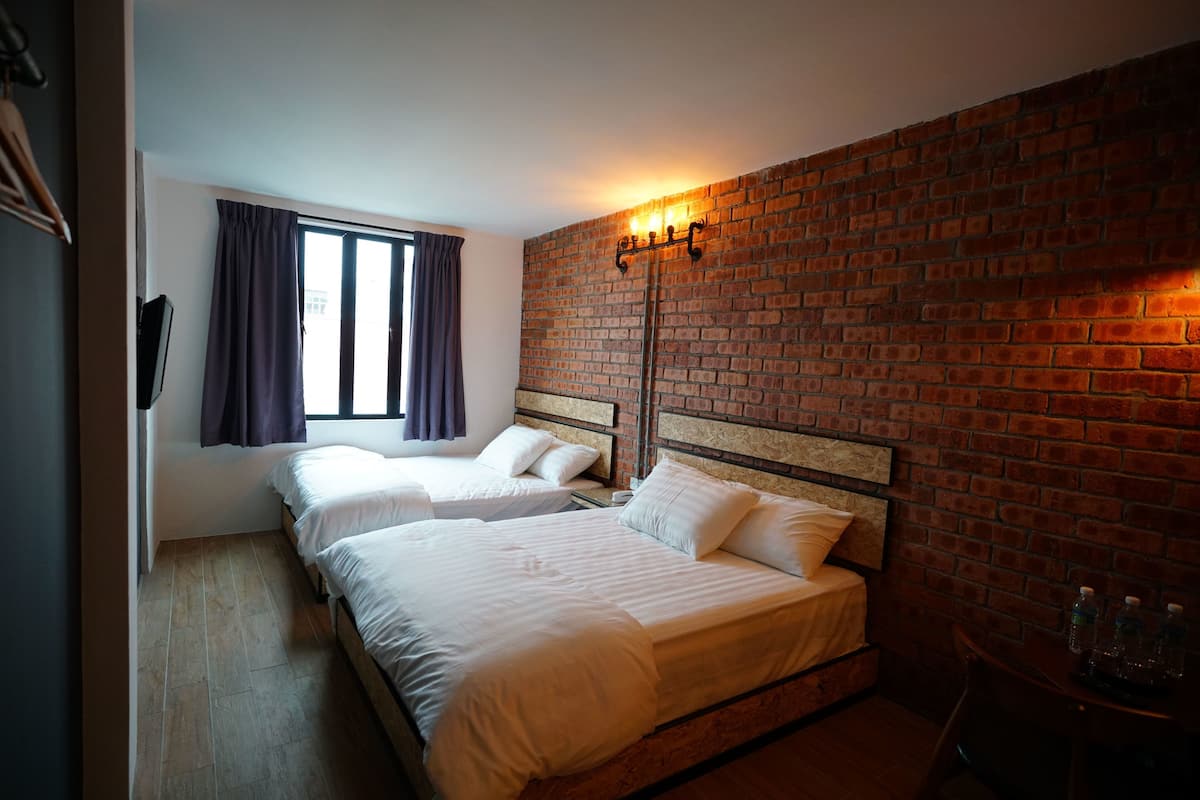A hotel room with two beds, a brick wall, and a window with curtains.