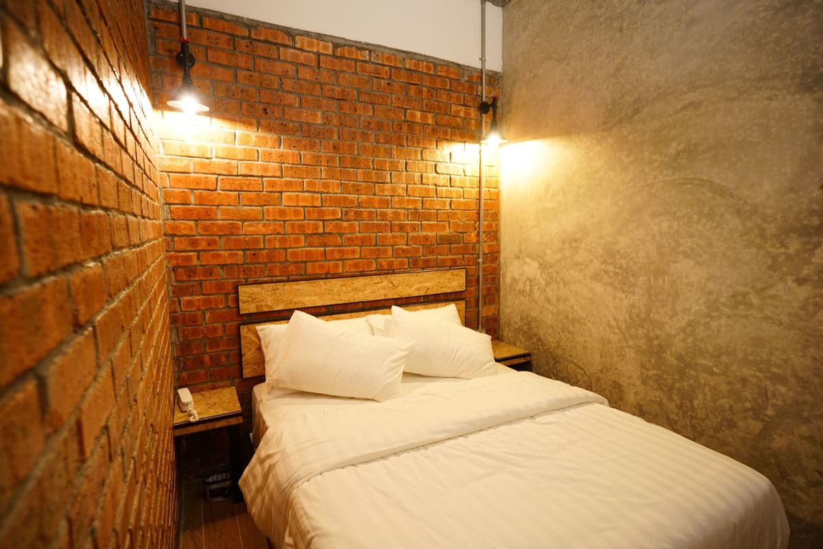 A hotel room with a brick wall, a wooden headboard, and a bed with white bedding.