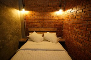 A bed with a wooden headboard in a room with brick walls and two bedside lamps.