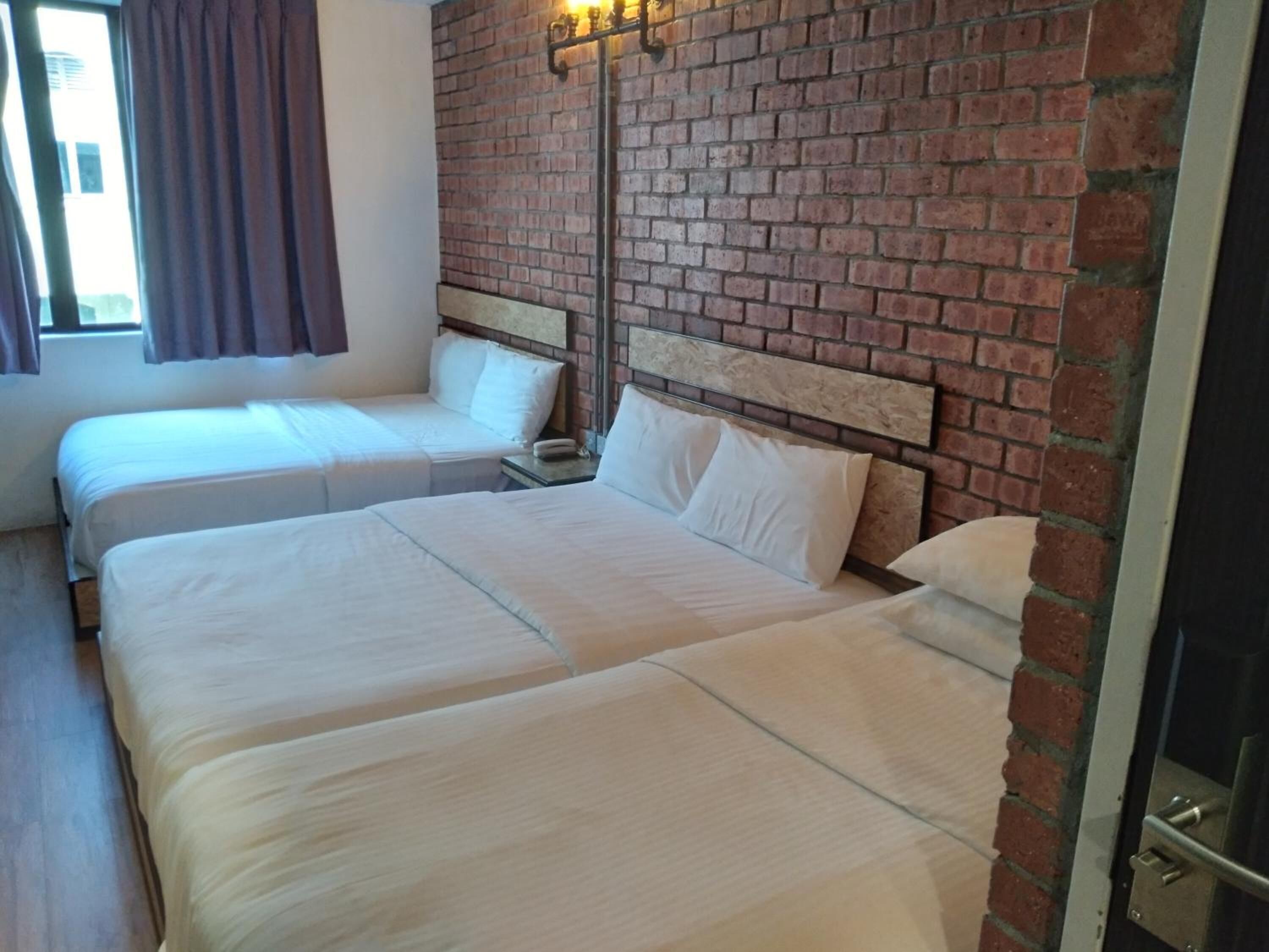 Una habitación de hotel con dos camas, una pared de ladrillo y una ventana con cortinas.