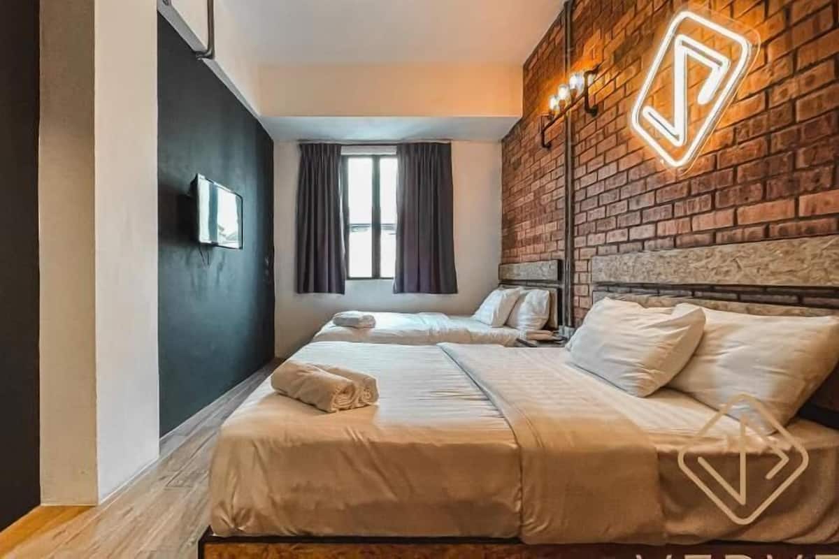 A hotel room with two beds, a brick accent wall, a window with curtains, and a wall-mounted light fixture.