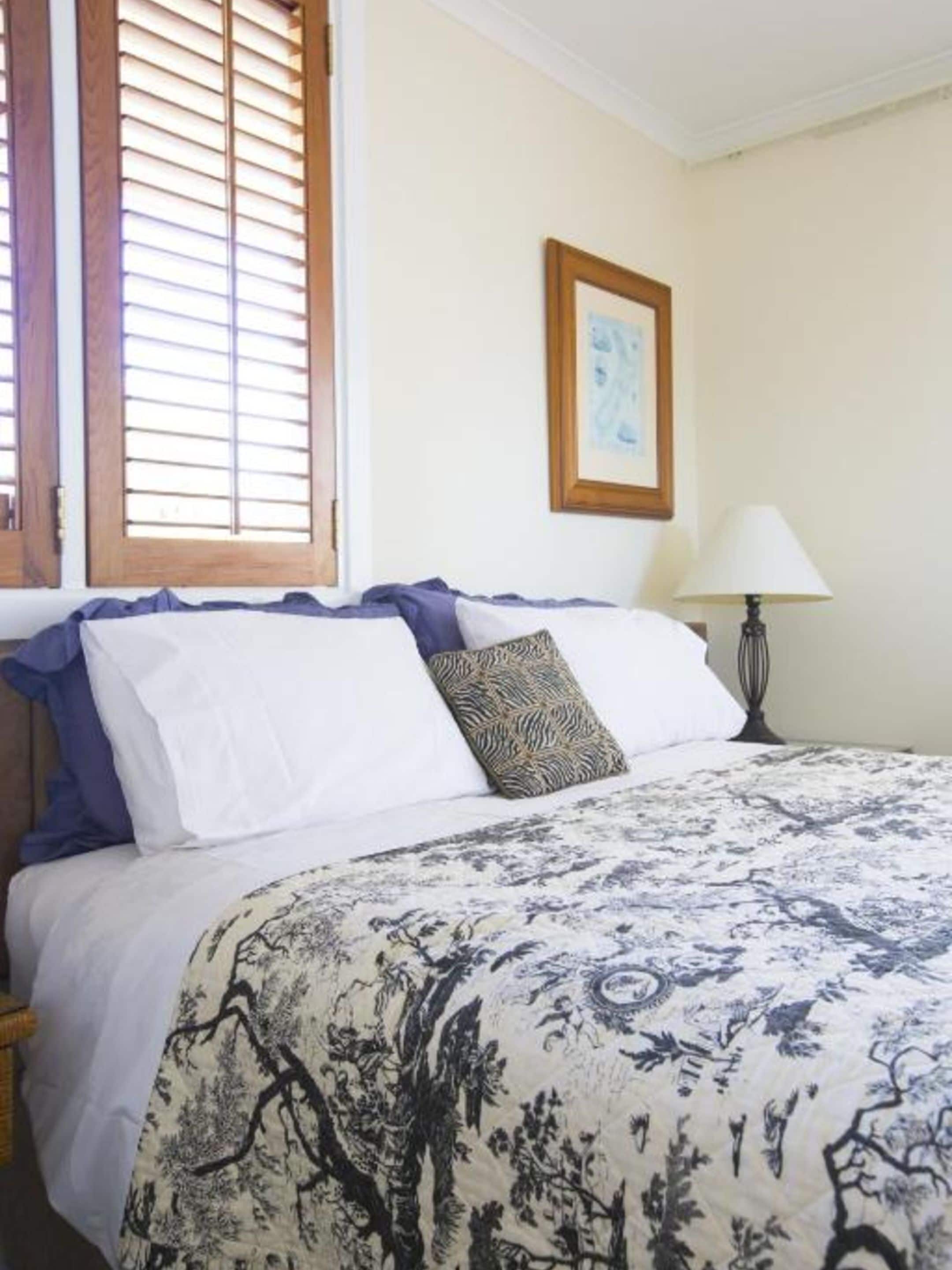 A neatly made bed with a patterned bedspread, a framed picture on the wall, and a lamp beside the bed.