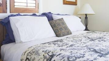 A neatly made bed with a patterned bedspread, a framed picture on the wall, and a lamp beside the bed.