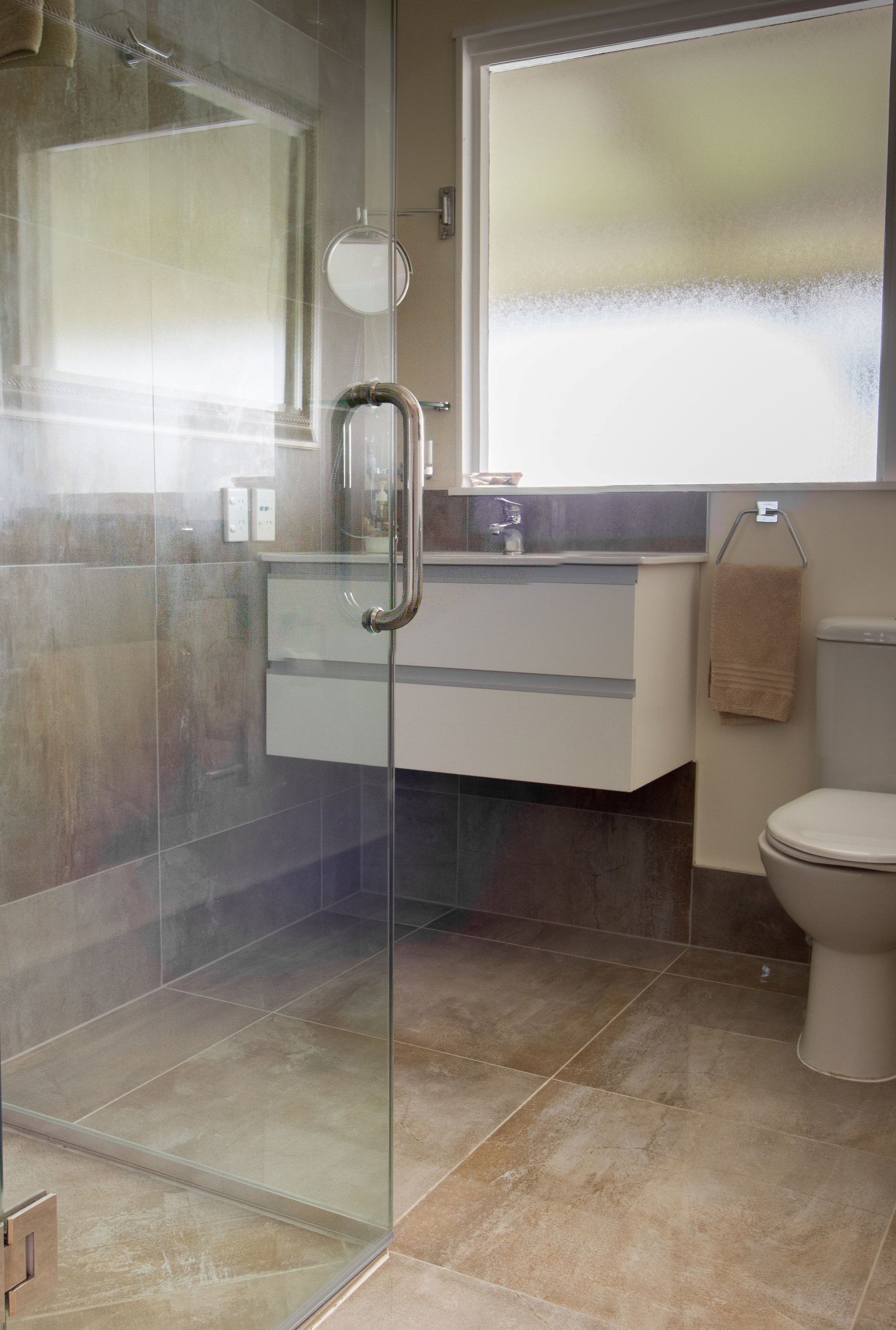 A modern bathroom with a glass-enclosed shower, a white toilet, and a vanity with a mirror.
