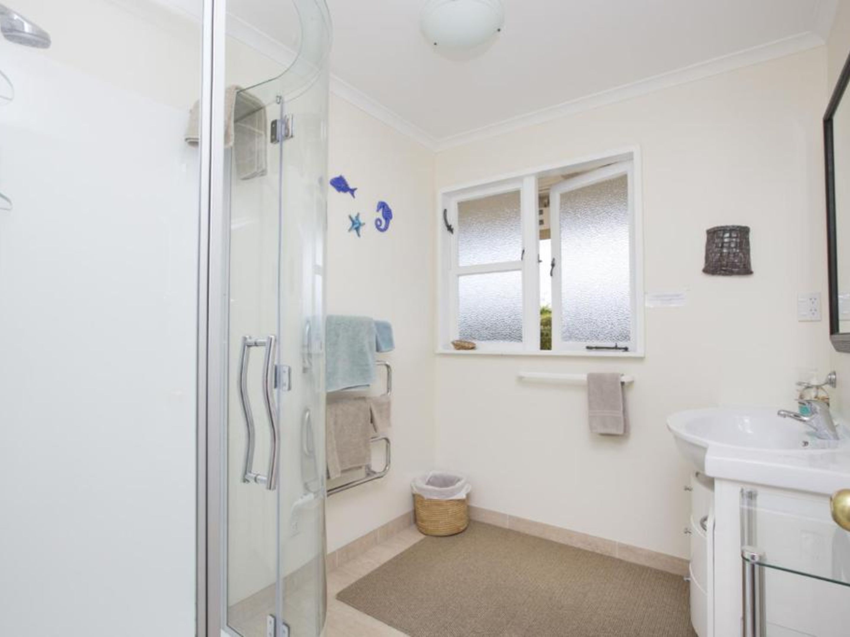 A bathroom with a glass shower enclosure, a sink with a mirror, and a window with frosted glass.