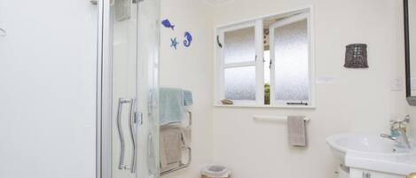 A bathroom with a glass shower enclosure, a sink with a mirror, and a window with frosted glass.
