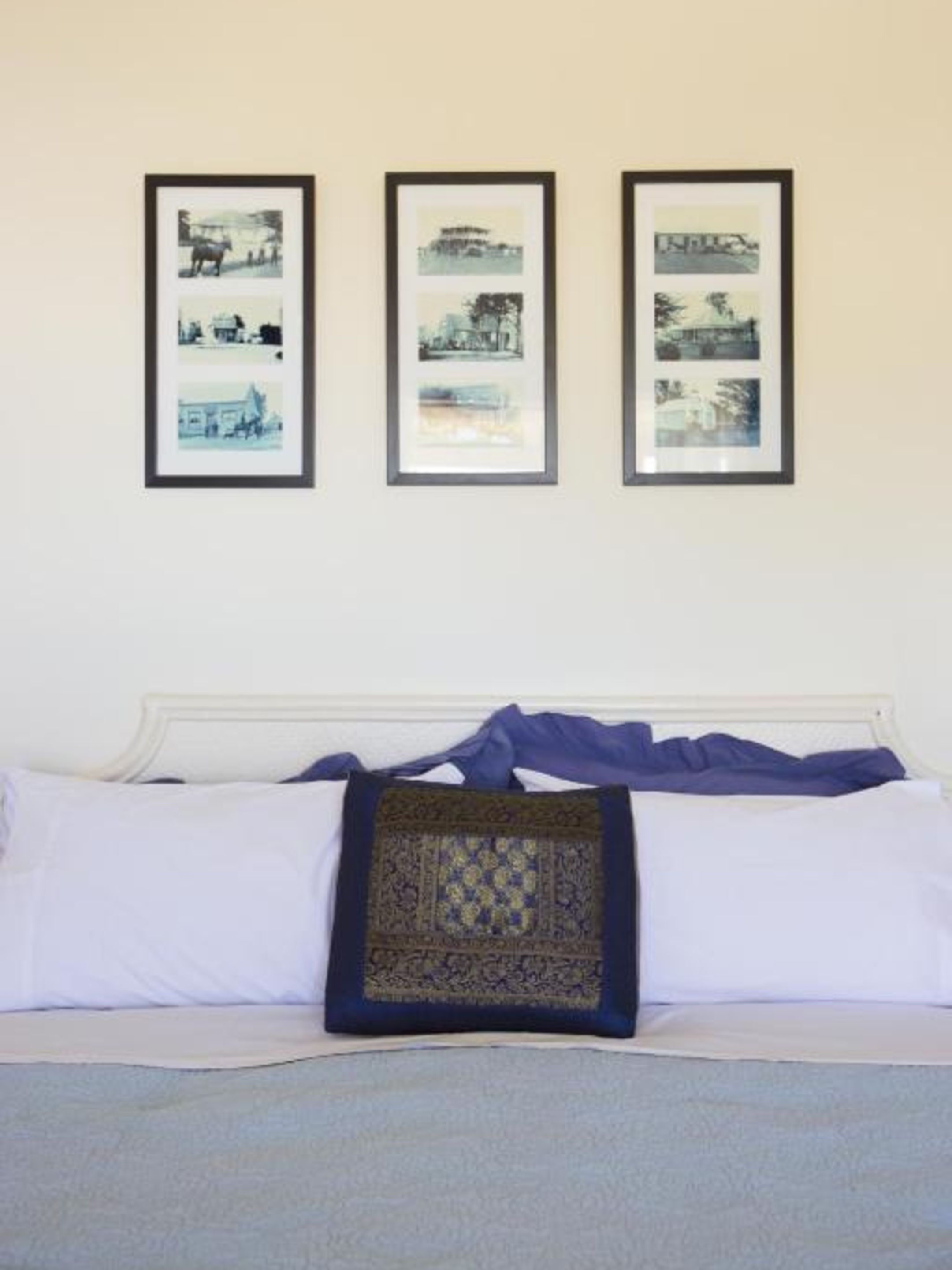 A bed with white linens and a single decorative pillow, flanked by three framed photographs on the wall.