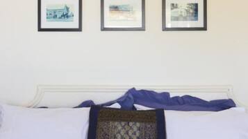 A bed with white linens and a single decorative pillow, flanked by three framed photographs on the wall.