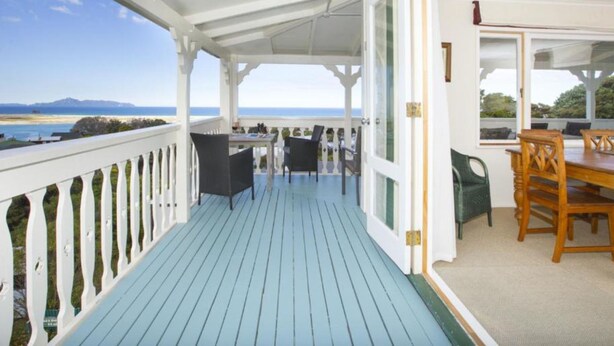 En overdækket terrasse udendørs med havudsigt, med et bord og stole.