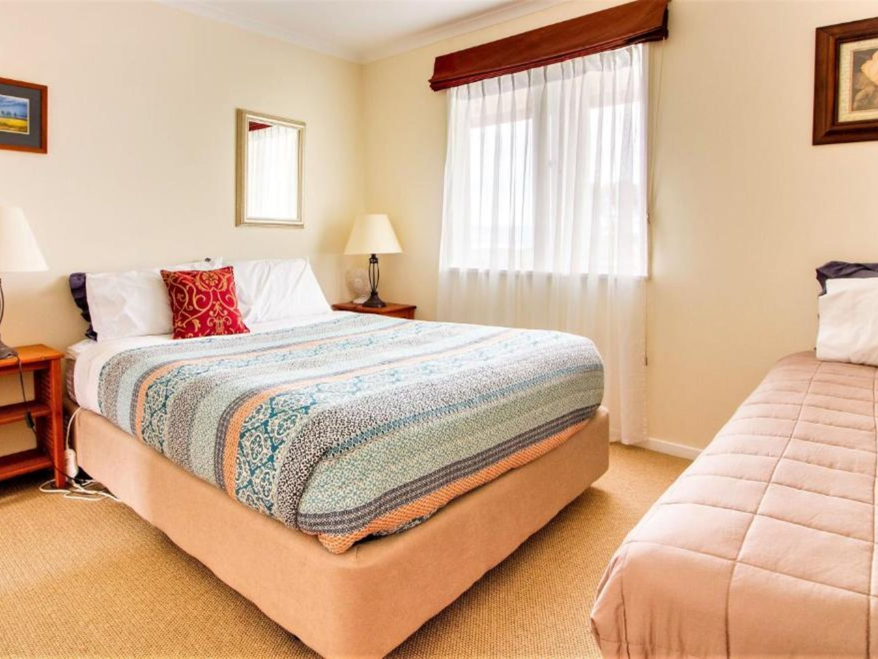 A hotel room with a large bed, a bedside table with a lamp, a window with sheer curtains, and a framed picture on the wall.