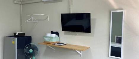 Une chambre dotée d’un téléviseur à écran plat fixé au mur, d’une petite table avec un ventilateur, un radiateur et un miroir.