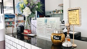 A hotel reception desk with a vase of flowers, a sign with room rates, and a 'tips' jar. - Baan Nuk Anong (Chiang Rai)
