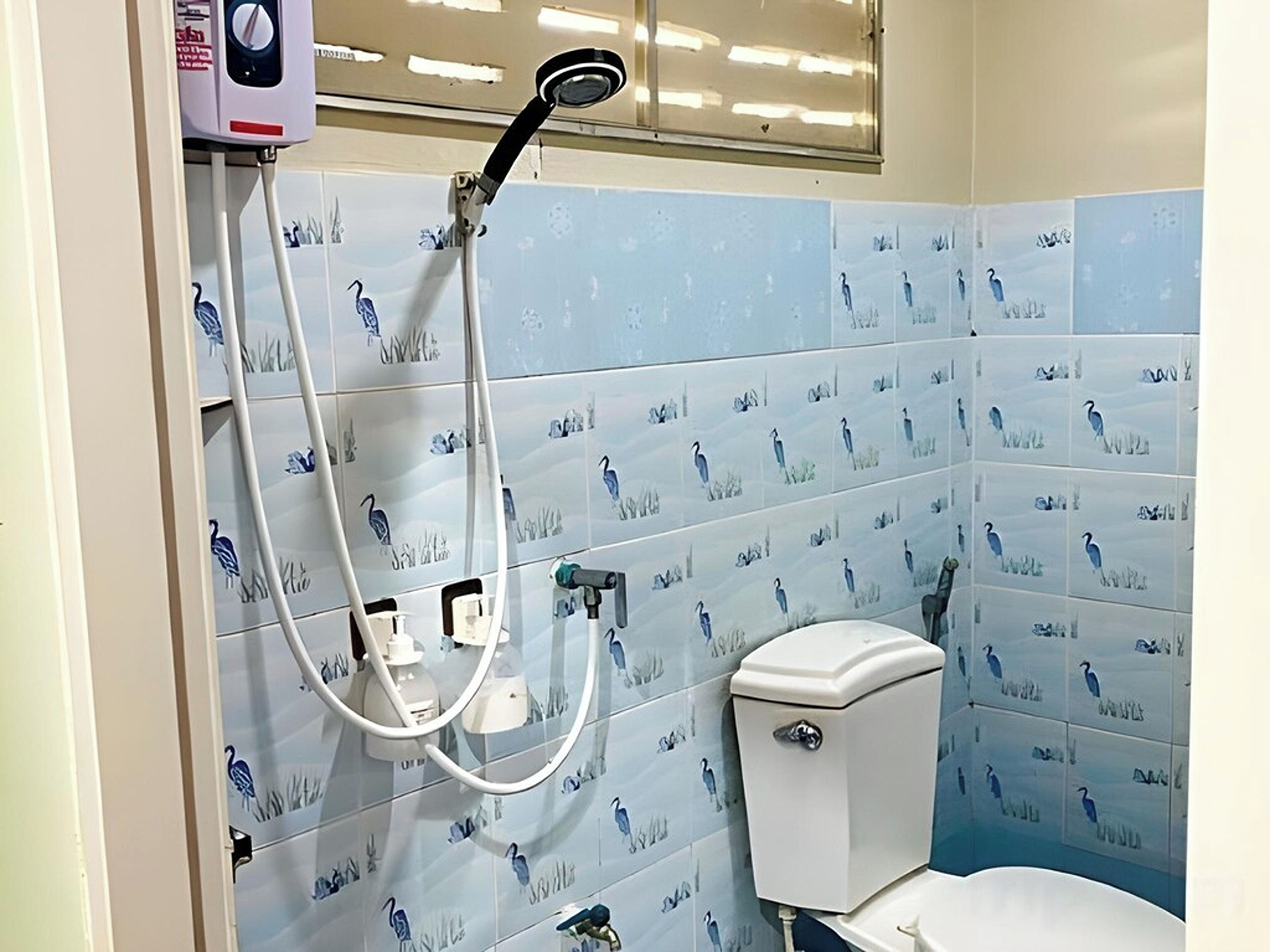 Un baño con azulejos azules con motivos de pájaros, un inodoro y una ducha con manguera.