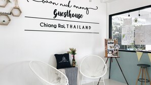 A modern guesthouse interior with a welcoming sign, two white chairs, a small table, and a window with a view of greenery. - Baan Nuk Anong (Chiang Rai)