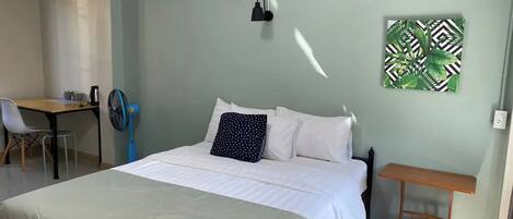 Un dormitorio con cama, escritorio, silla, una mesita y un ventilador de pared.