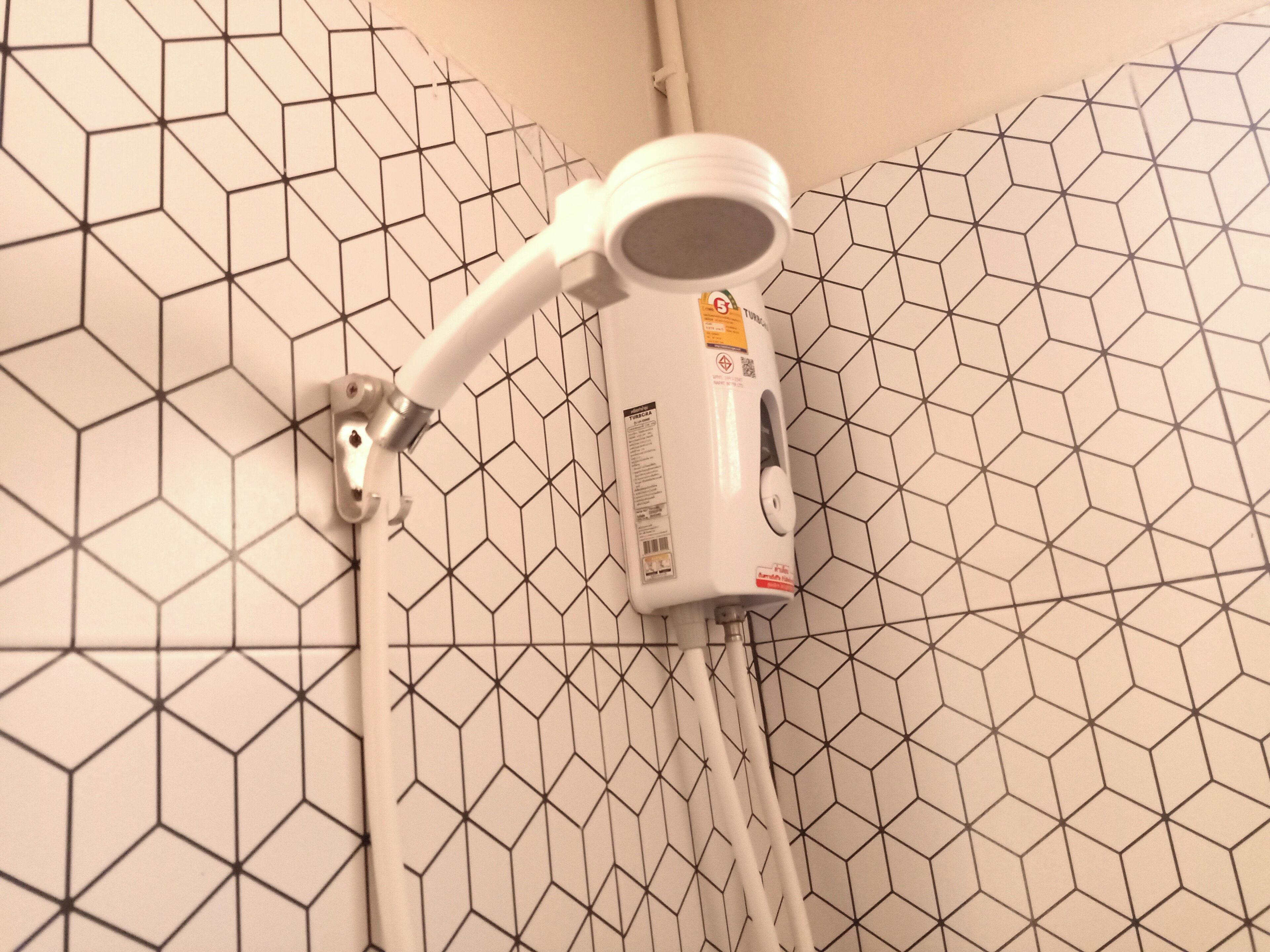 A shower with a white handheld showerhead mounted on a wall with a geometric tile pattern.