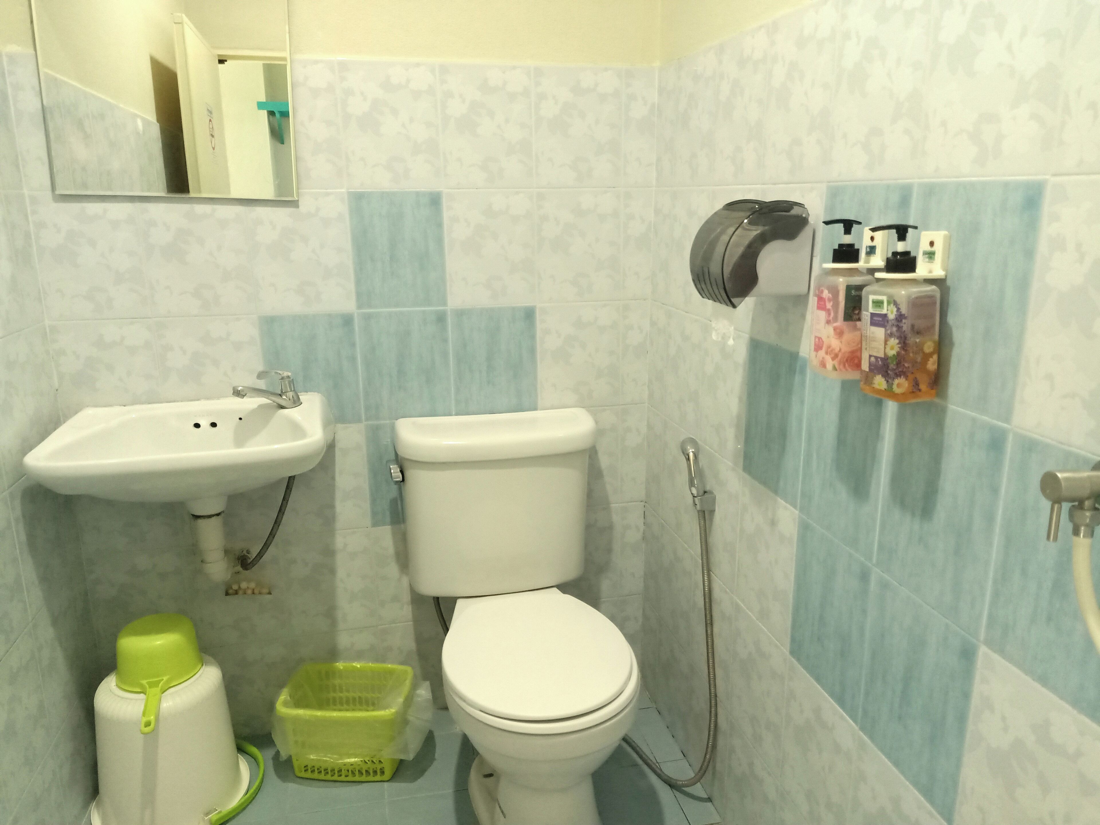 A bathroom with a sink, toilet, and shower. There are toiletries on the wall and a green basket on the floor.