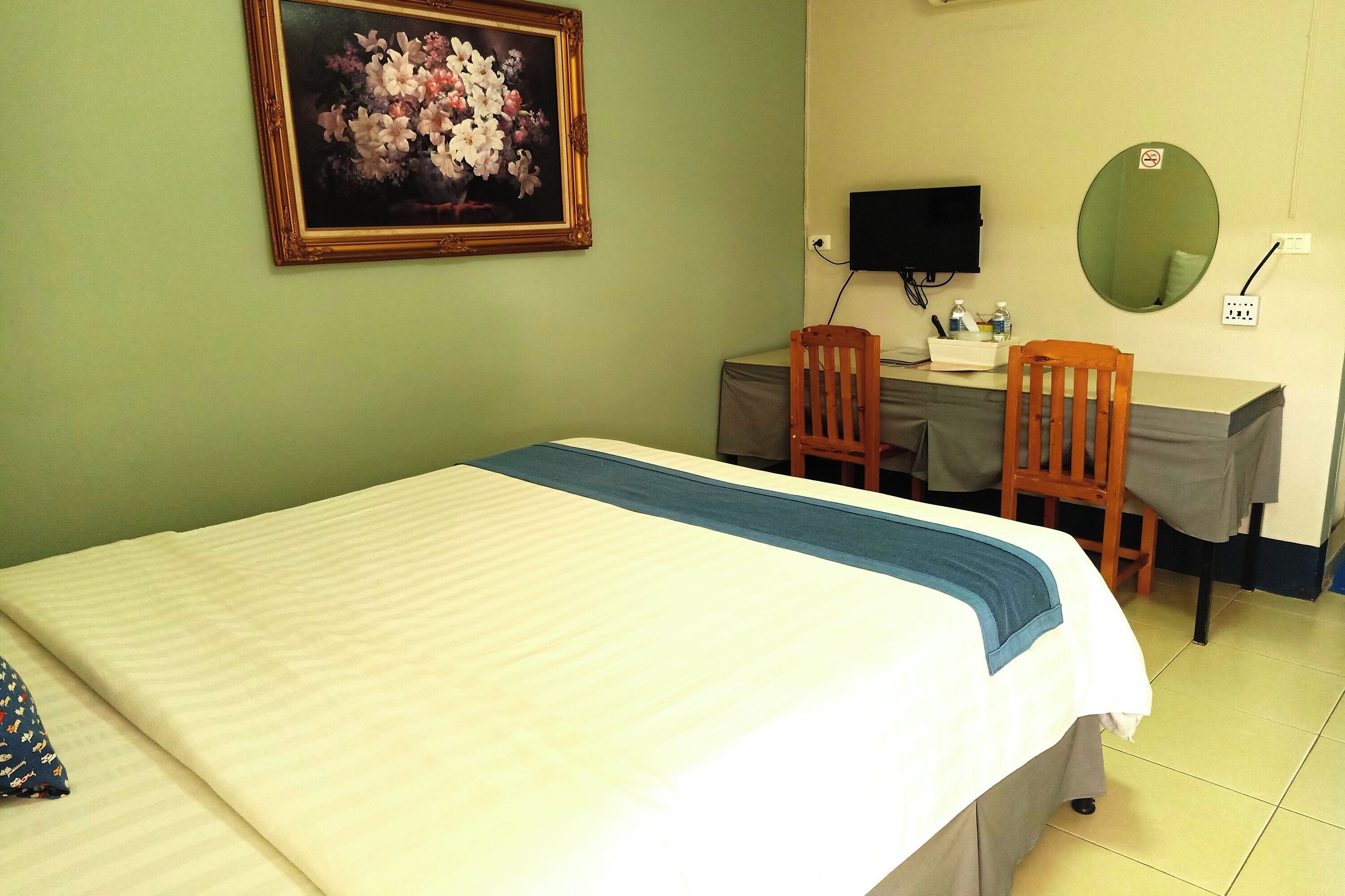 A hotel room with a bed, a desk, two chairs, a television, a mirror, and a painting on the wall.