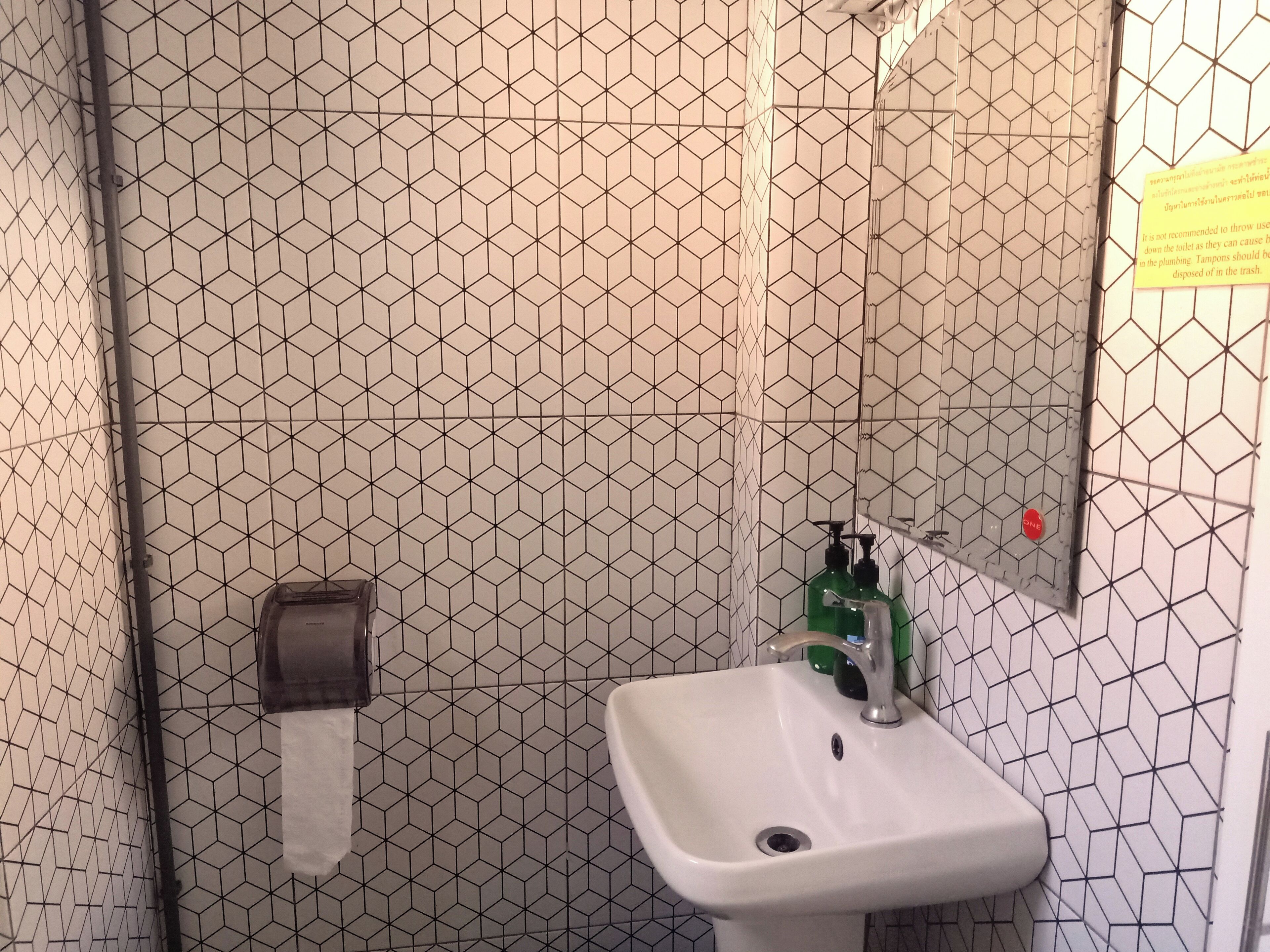 Une salle de bain avec un lavabo blanc, un distributeur d’essuie-tout et un distributeur de savon vert.
