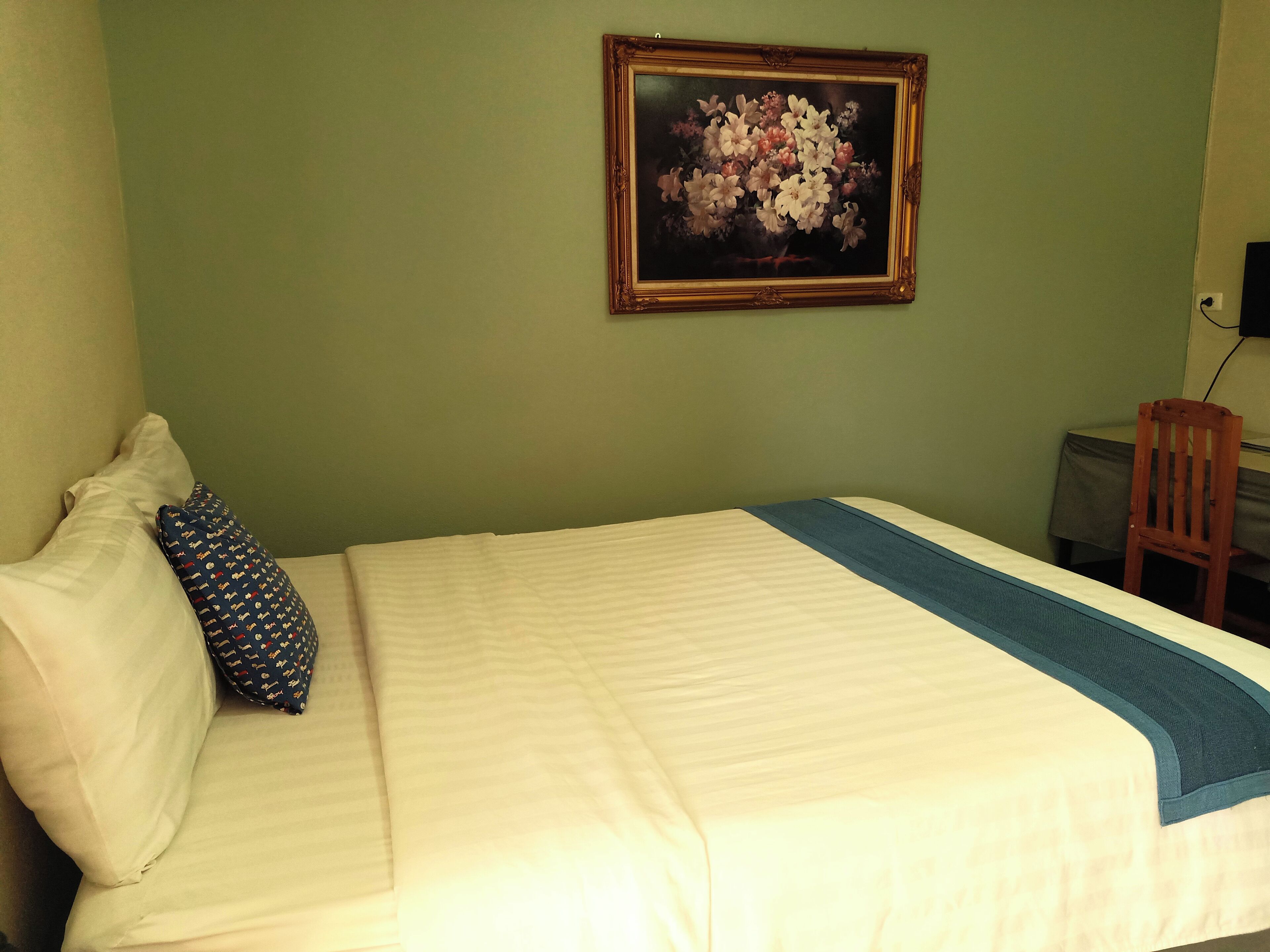 A hotel room with a bed, pillows, a framed floral artwork on the wall, and a chair.