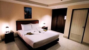 A hotel room with a large bed, two bedside tables with lamps, a nightstand, a painting on the wall, and a door. - Rayong Lanna Hotel (Rayong)