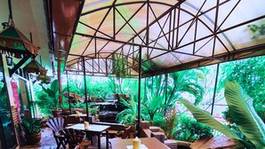 An outdoor patio with wooden tables and chairs, surrounded by lush greenery and a water feature. - Rayong Lanna Hotel (Rayong)