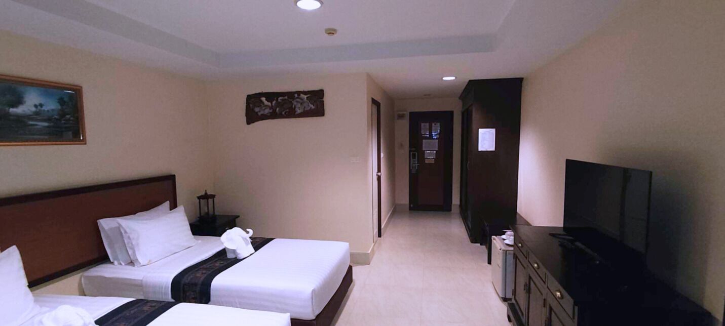 A hotel room with two beds, a television, and a hallway leading to a door.