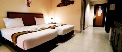 A hotel room with two beds, each with white linens and a brown headboard. There is a nightstand with a lamp between the beds.