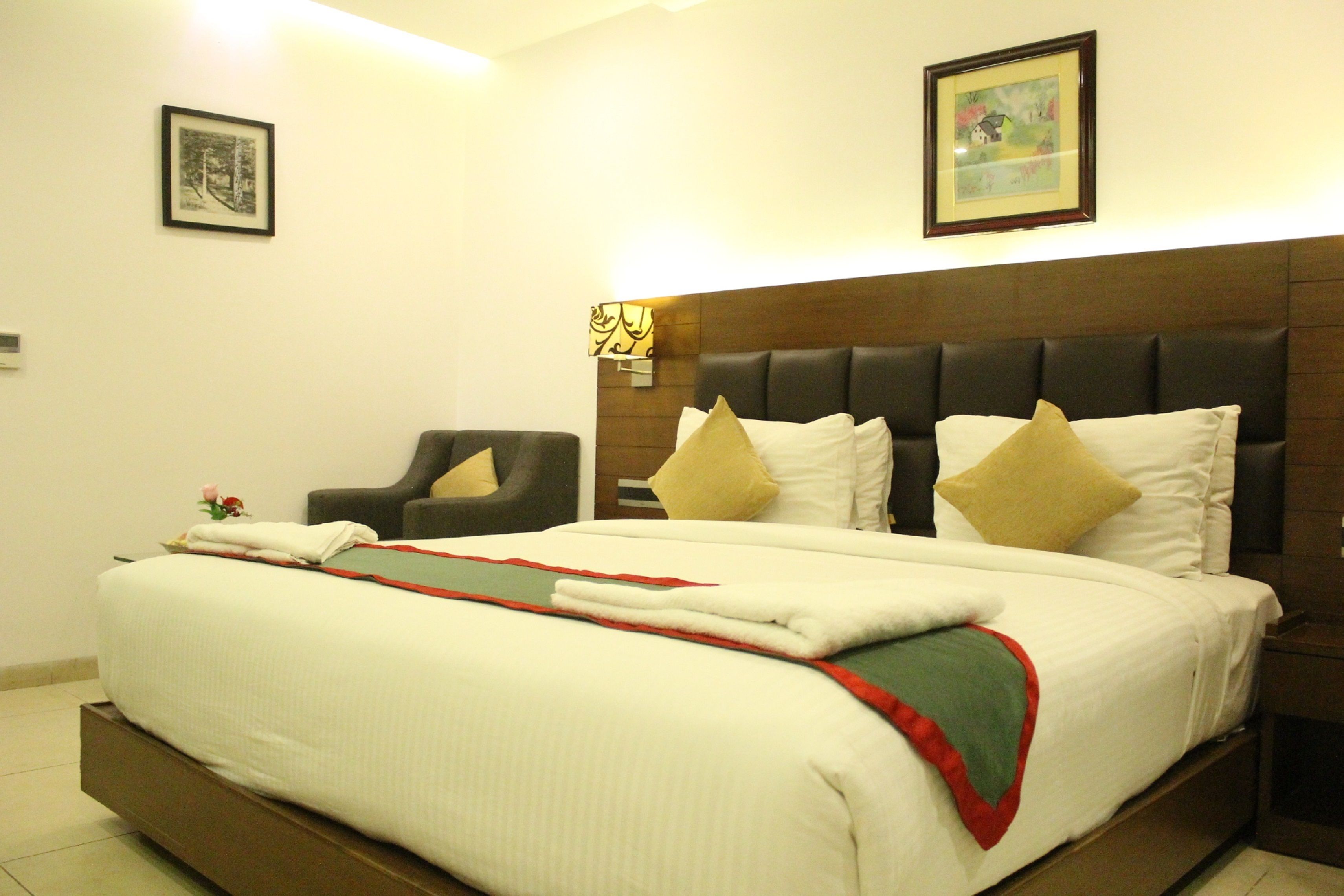 A neatly made bed with a red and green throw, a chair, and a nightstand with a lamp.