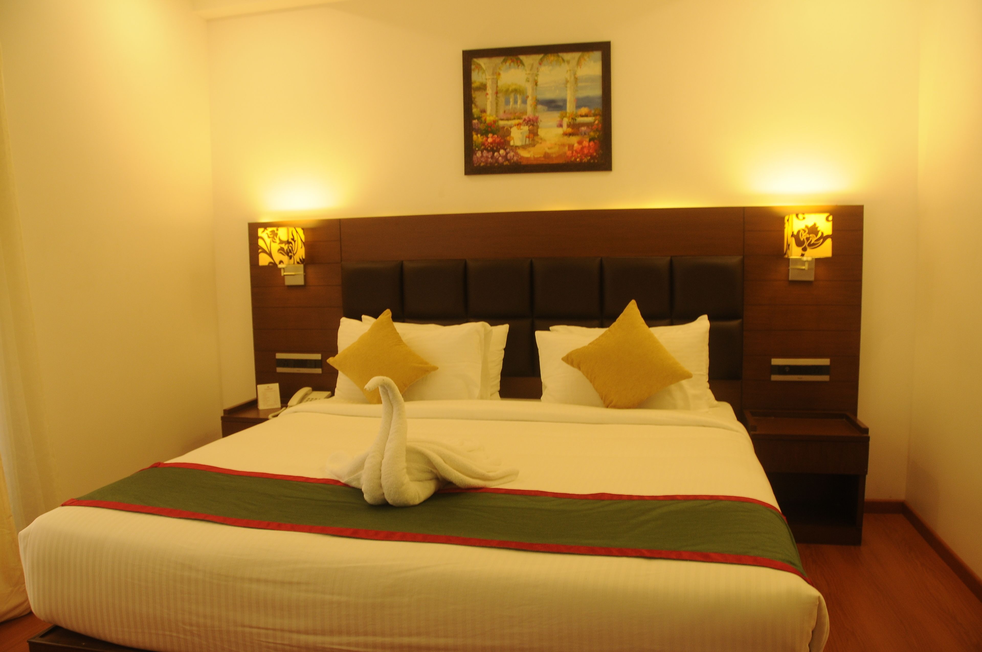 A hotel room with a large bed, two bedside lamps, a painting on the wall, and a swan-shaped pillow.