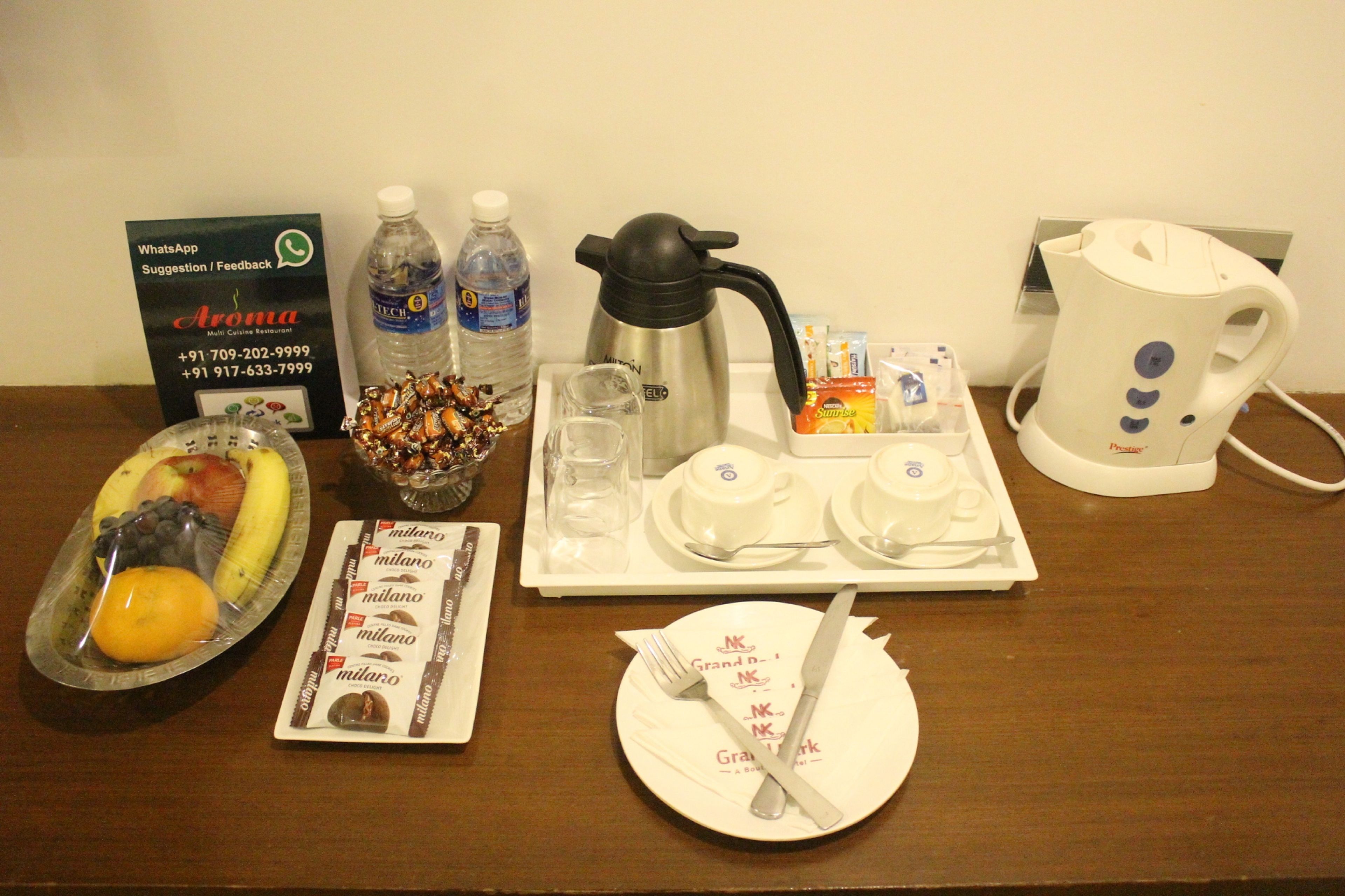 A breakfast setup with a tray of food, including fruits, a bottle of water, a coffee maker, and a teapot.