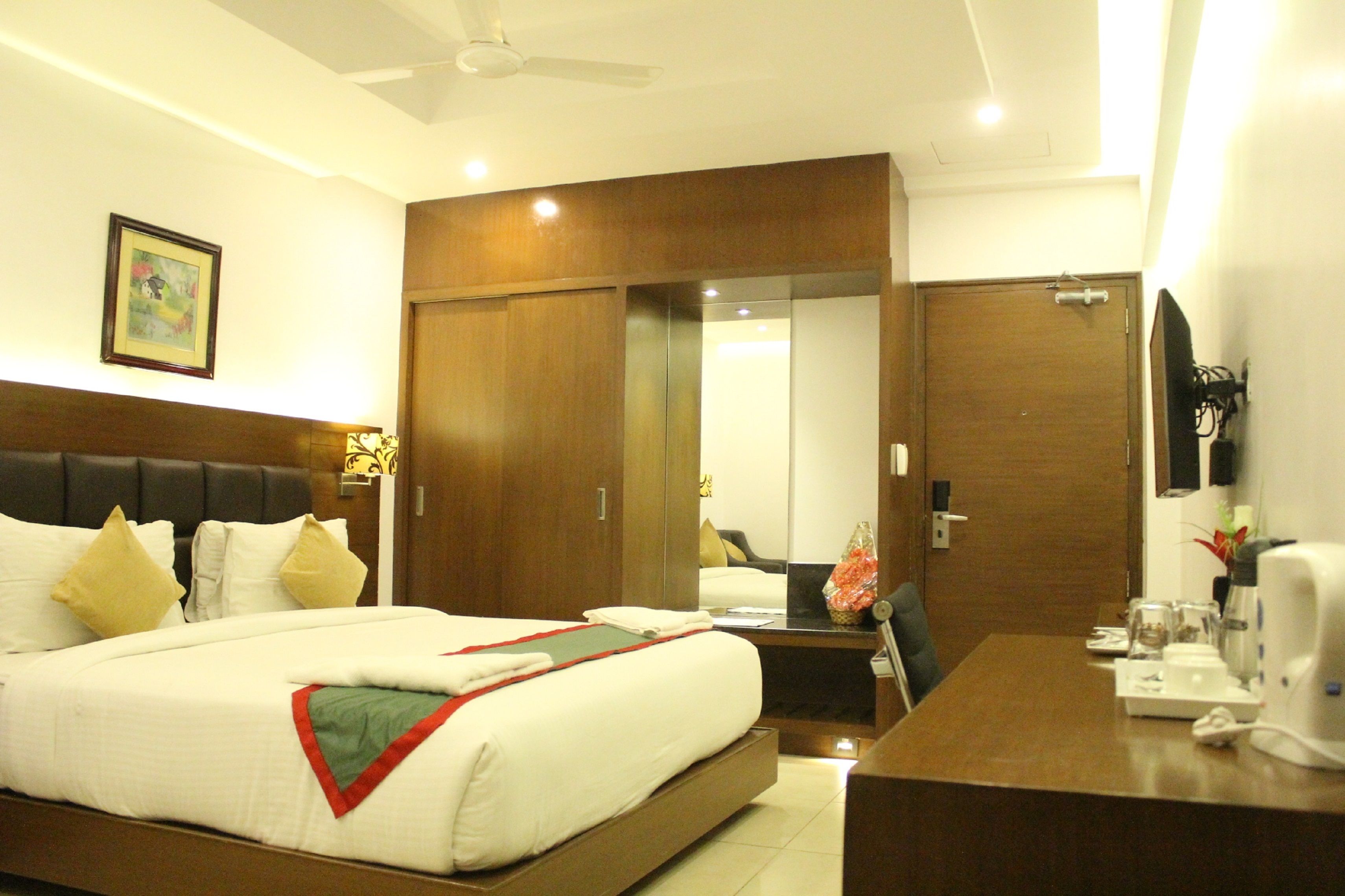 A hotel room with a large bed, a desk with a coffee maker, a mirror, and a wardrobe.