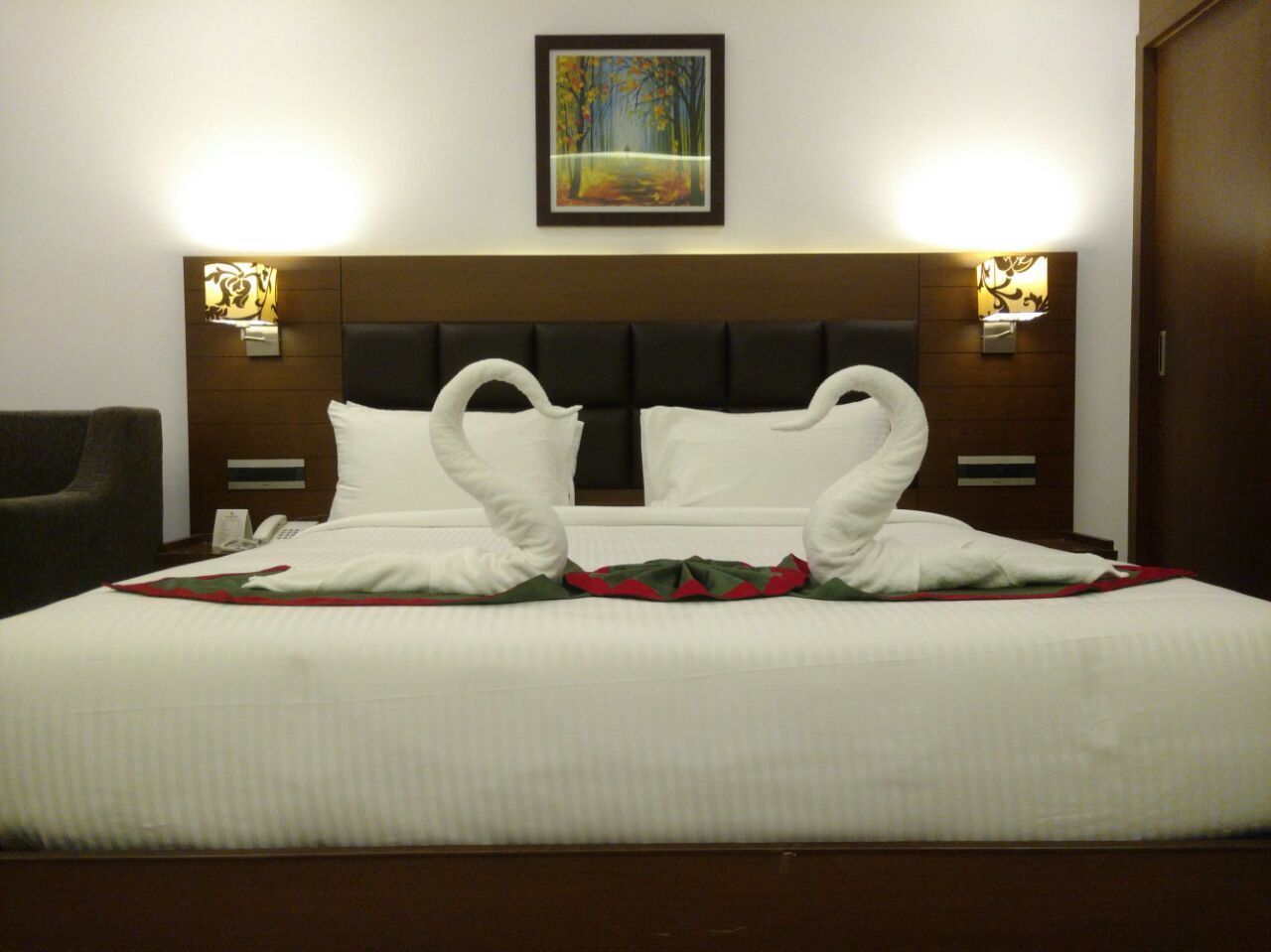 Una habitación de hotel con una cama grande, dos lámparas adosadas a la pared, un cuadro sobre la cama y un cabecero de madera.