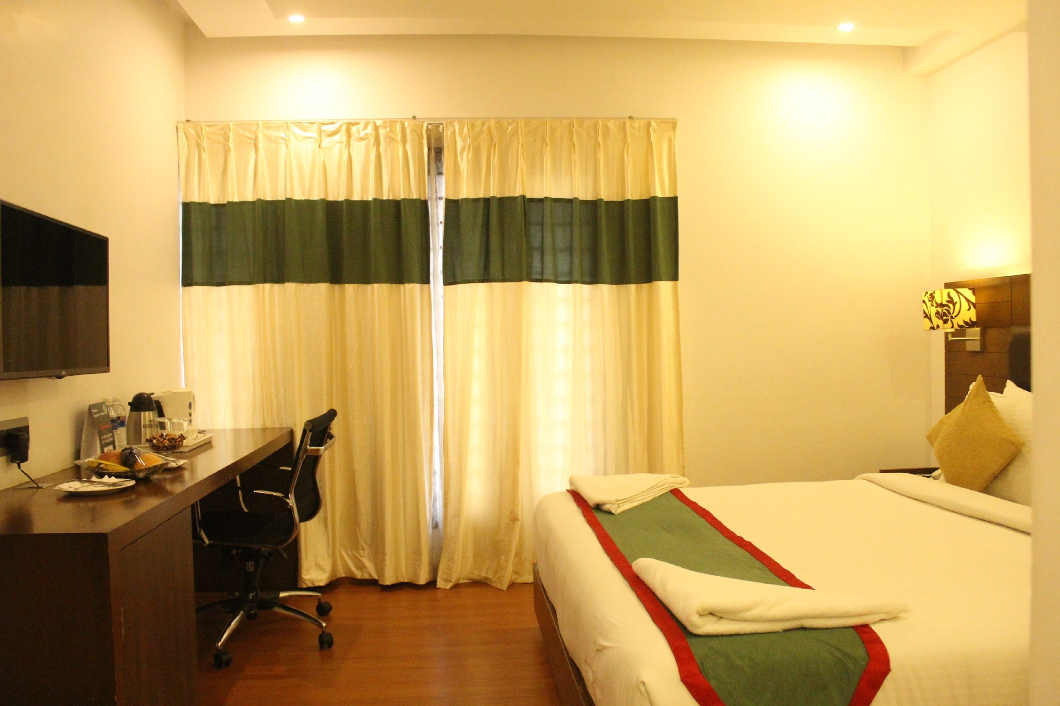 Une chambre d’hôtel équipée d’un lit, d’un bureau, d’une chaise et d’un téléviseur fixé au mur.