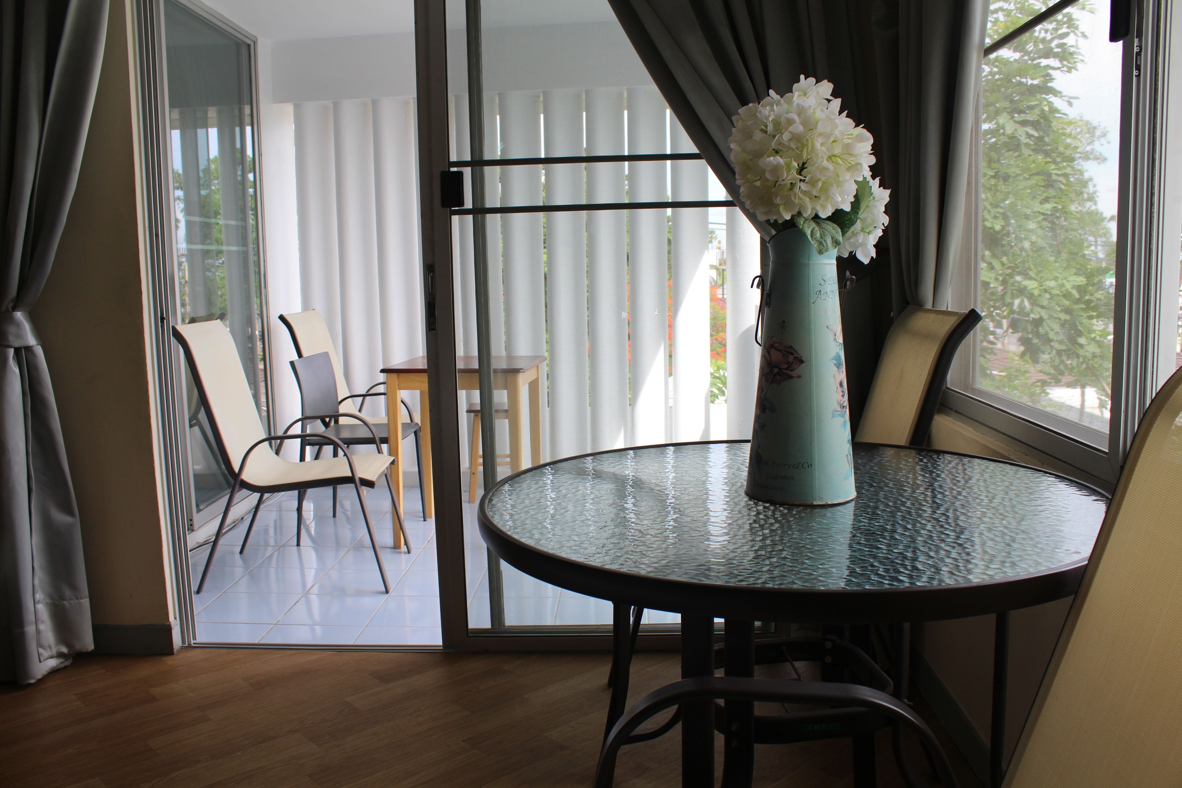 Ein Zimmer mit einem runden Glastisch, einer Blumenvase und Blick durch eine Glastür auf einen Außenbereich mit Sitzgelegenheiten.