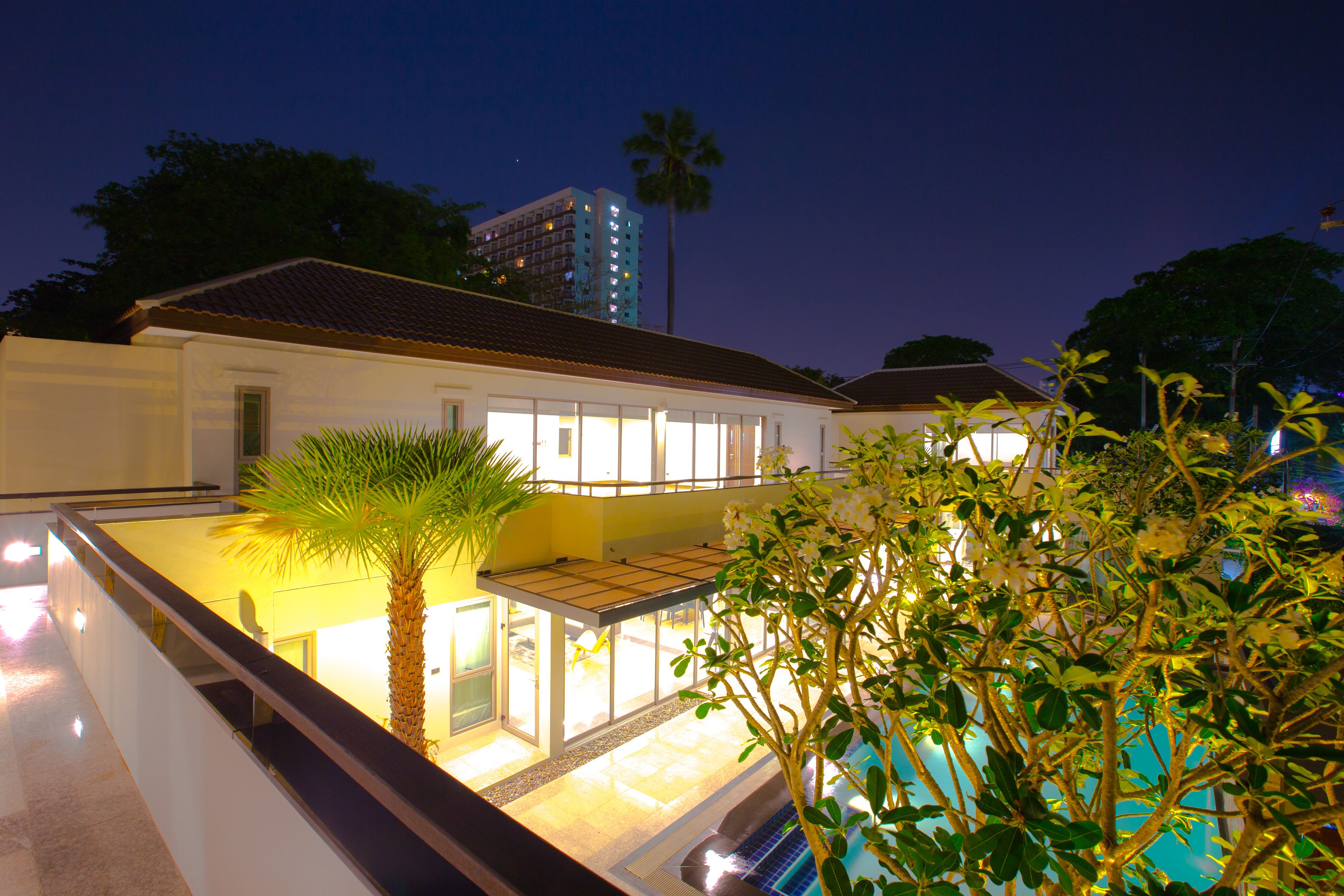 A modern hotel with a pool, a palm tree, and a view of a tall building in the background.