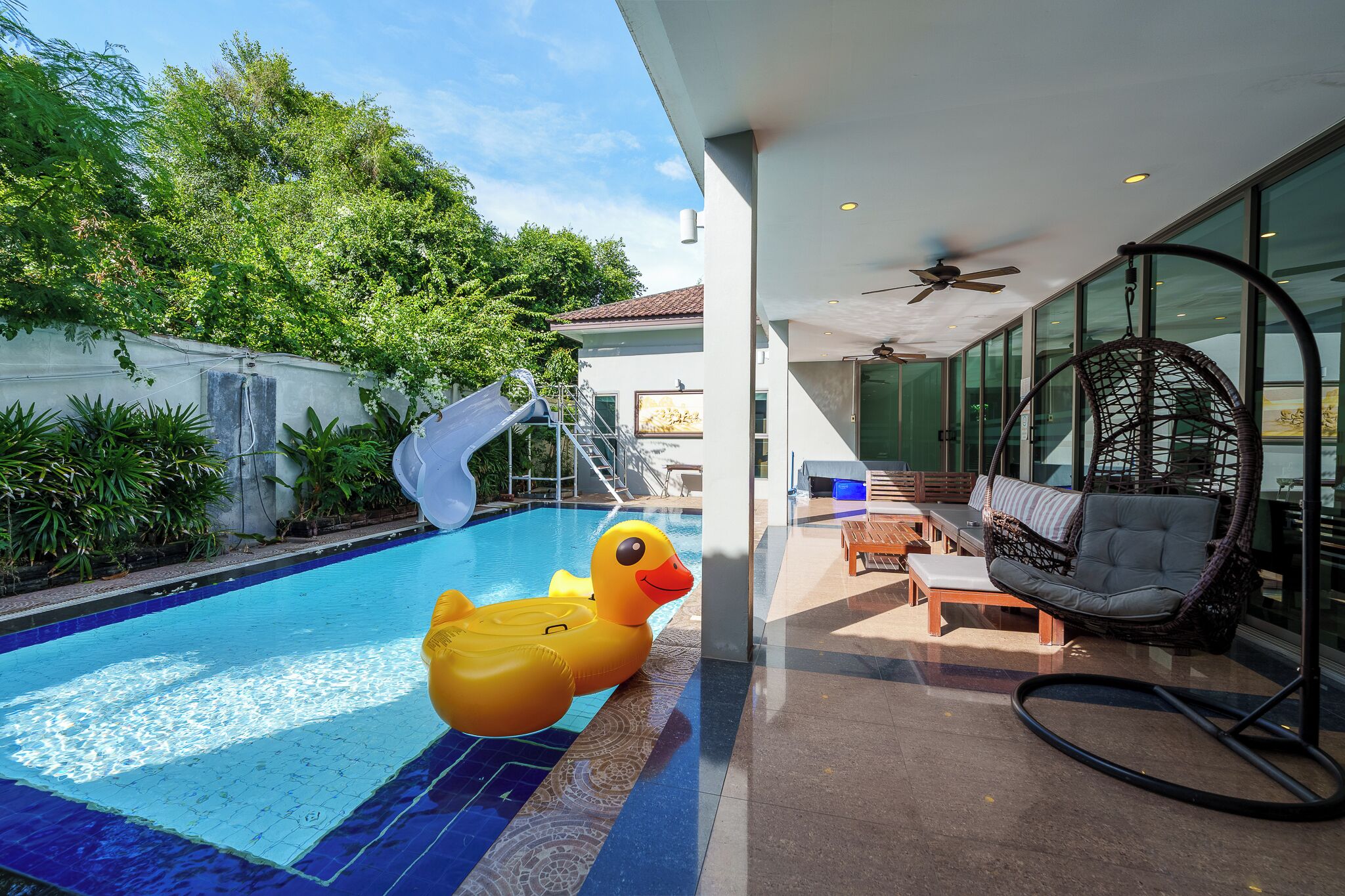 Une piscine avec un flotteur en forme de canard, un ventilateur de plafond et une chaise en osier.