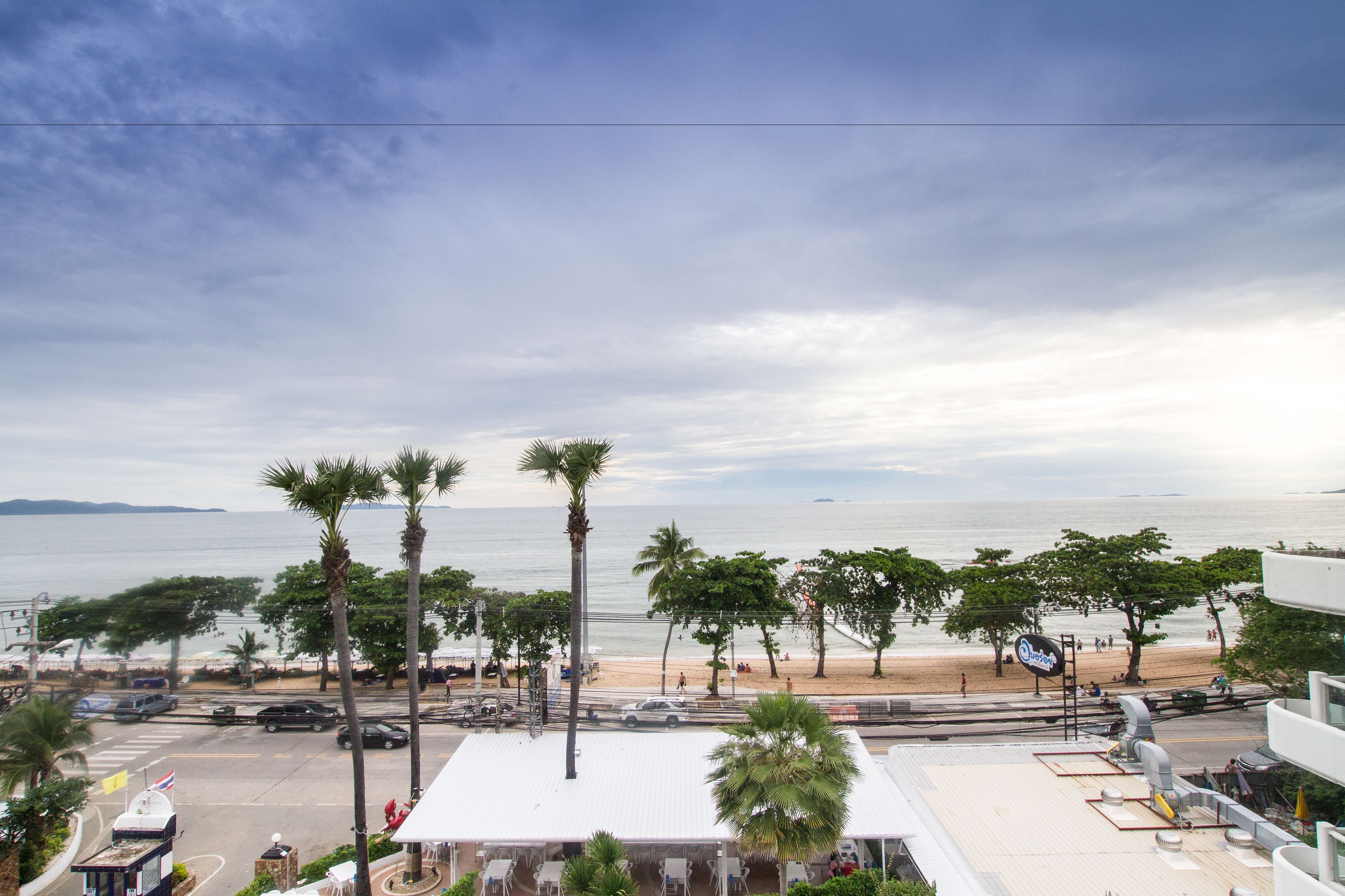Vista de la playa con palmeras, una carretera y un edificio con techo blanco.